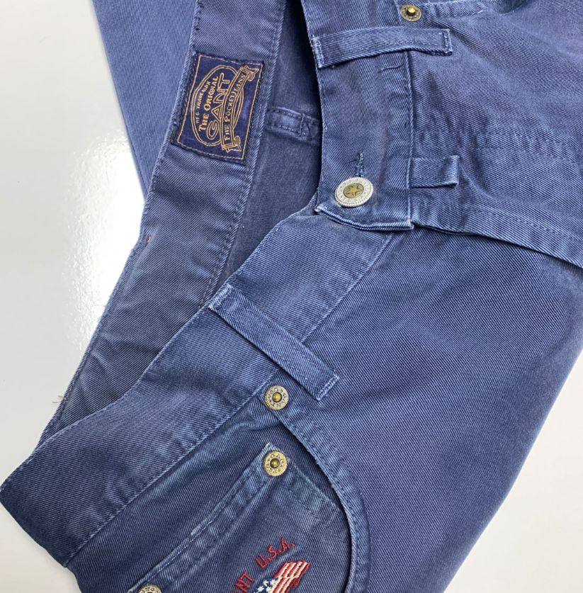 Close-up of blue denim pants with brand logo and buttons on a white background