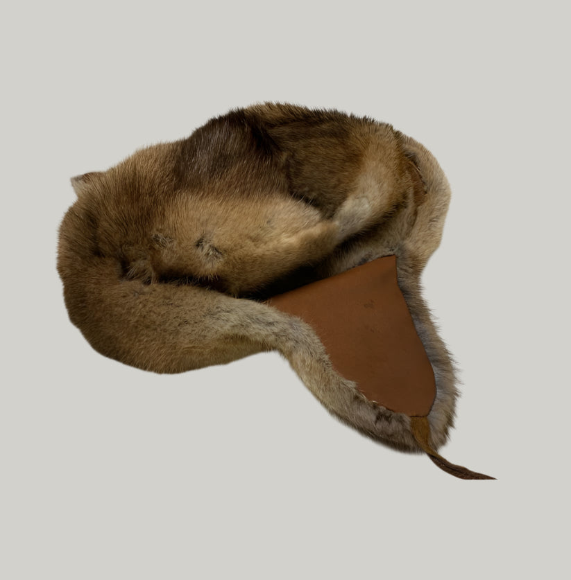 Brown fur hat with leather strap on a light gray floor