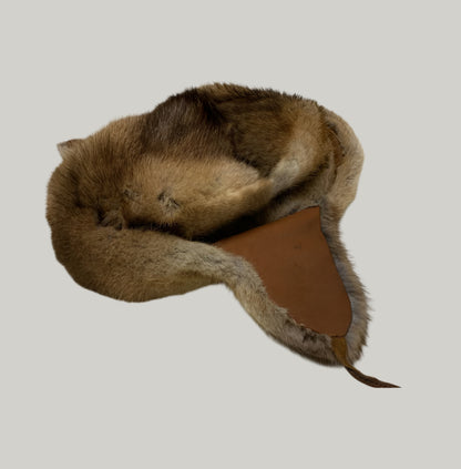 Brown fur hat with leather strap on a light gray floor