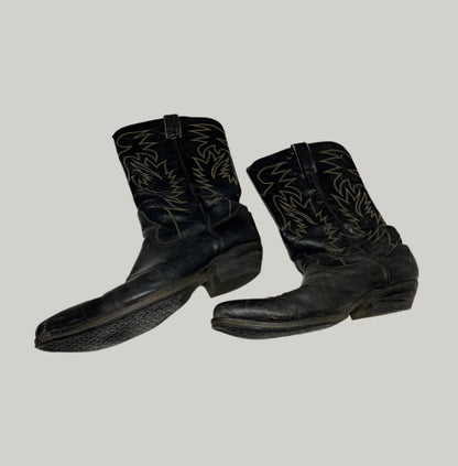 Pair of black cowboy boots with white embroidery on a light gray floor.