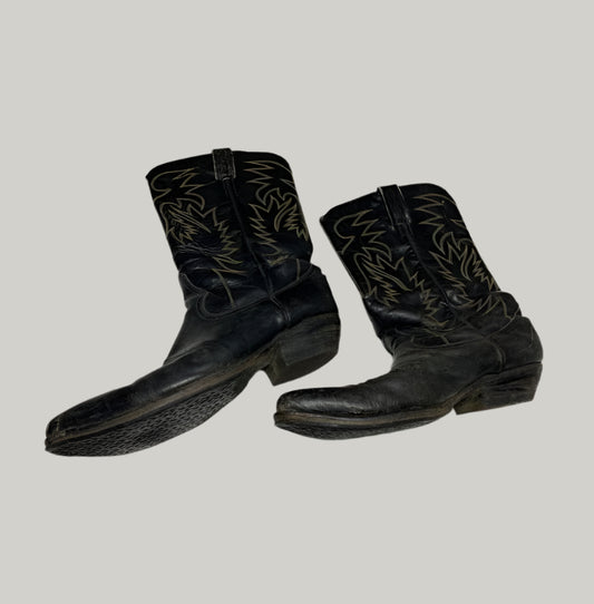 Pair of black cowboy boots with white embroidery on a light gray floor.