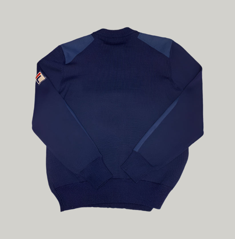 Navy blue sweater with a small logo on the sleeve against a light gray background