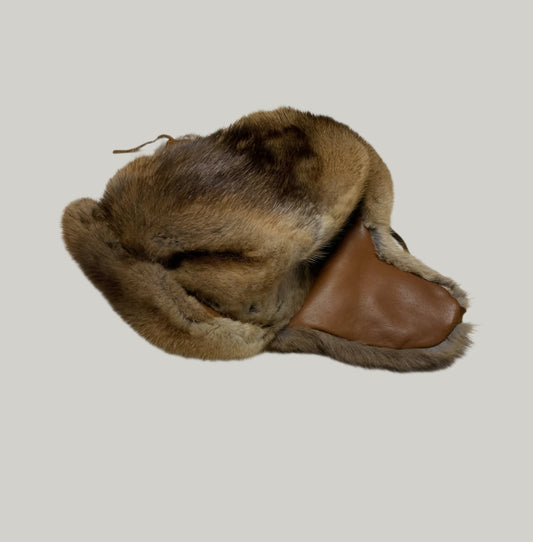 Brown fur hat with leather brim on a light gray floor